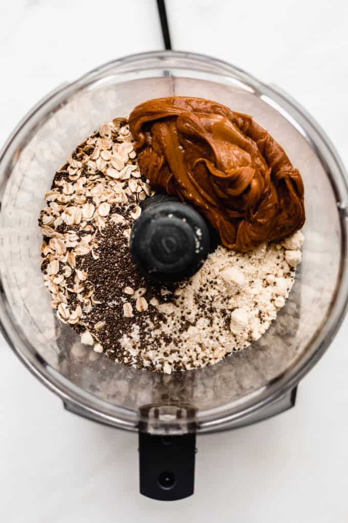 A food processor with oats, almond flour, chia seeds, peanut butter and maple syrup