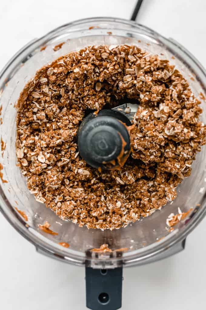 A food processor with blended oats, almond flour and peanut butter in it