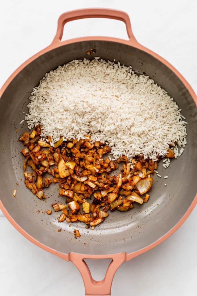 A pan with onions, garlic and white rice in it