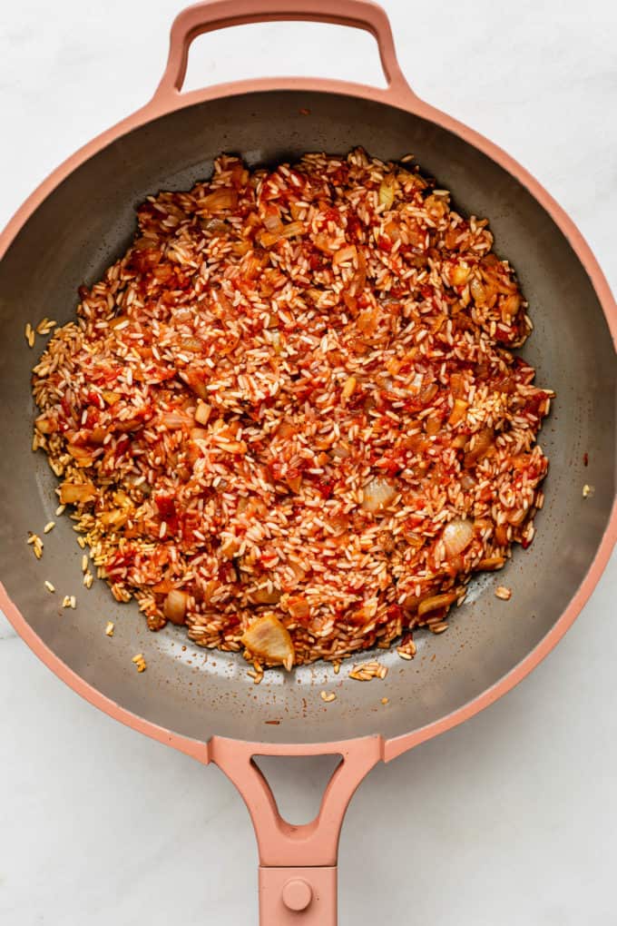 A pan with crushed tomatoes, rice and onions in it
