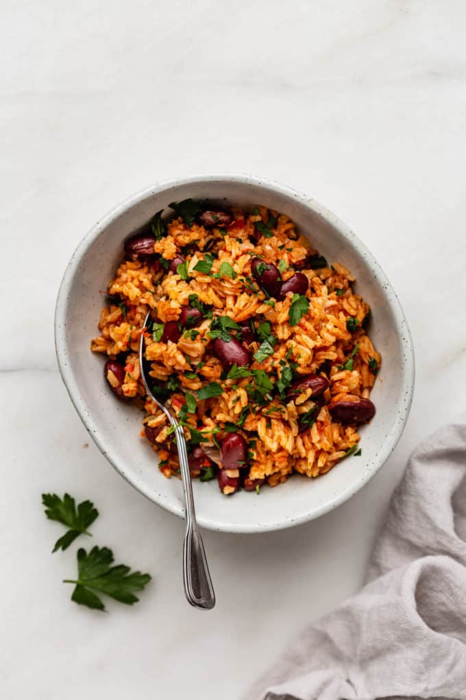A bowl of Spanish rice and beans with a spoon in it and a napkin on the side