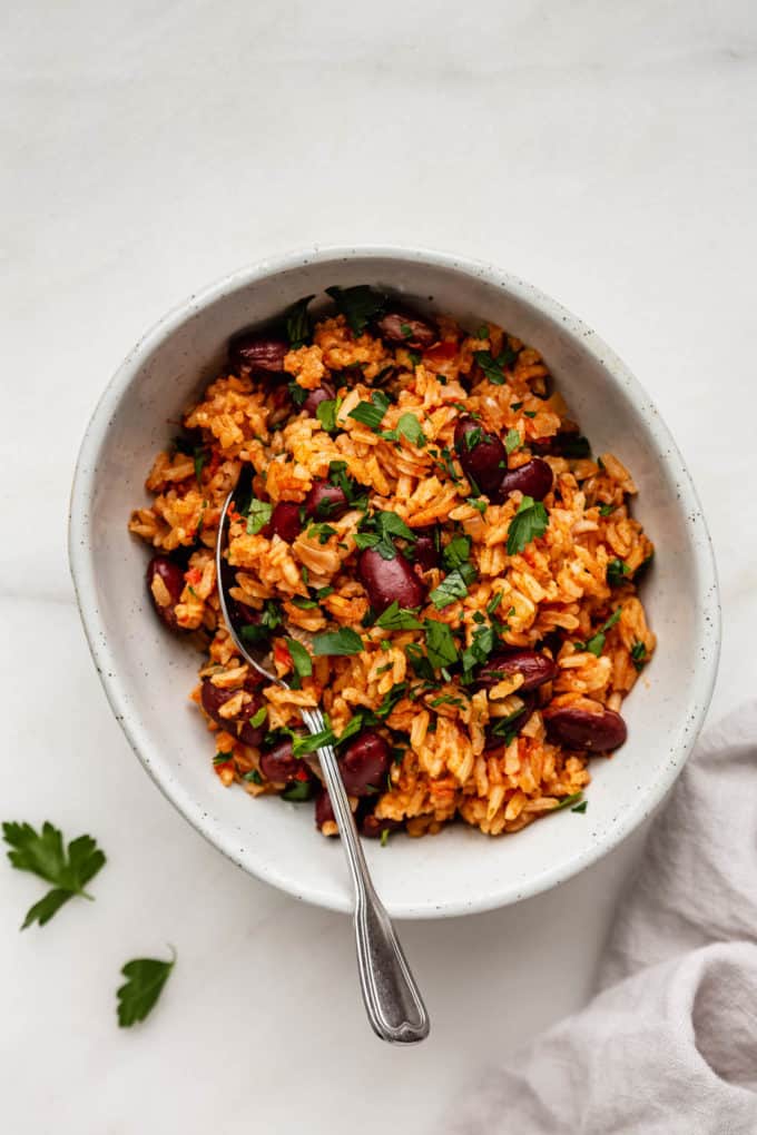 Spanish rice and beans in a bowl with parsley on top and a spoon i it