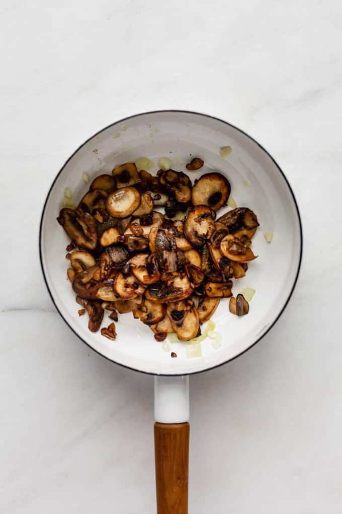 A white pot with sautéed mushrooms in it