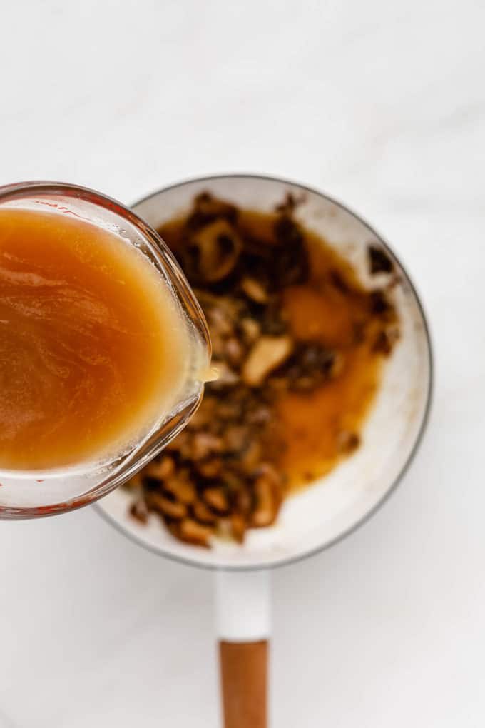 A measuring cup of veggie broth being poured into a pot