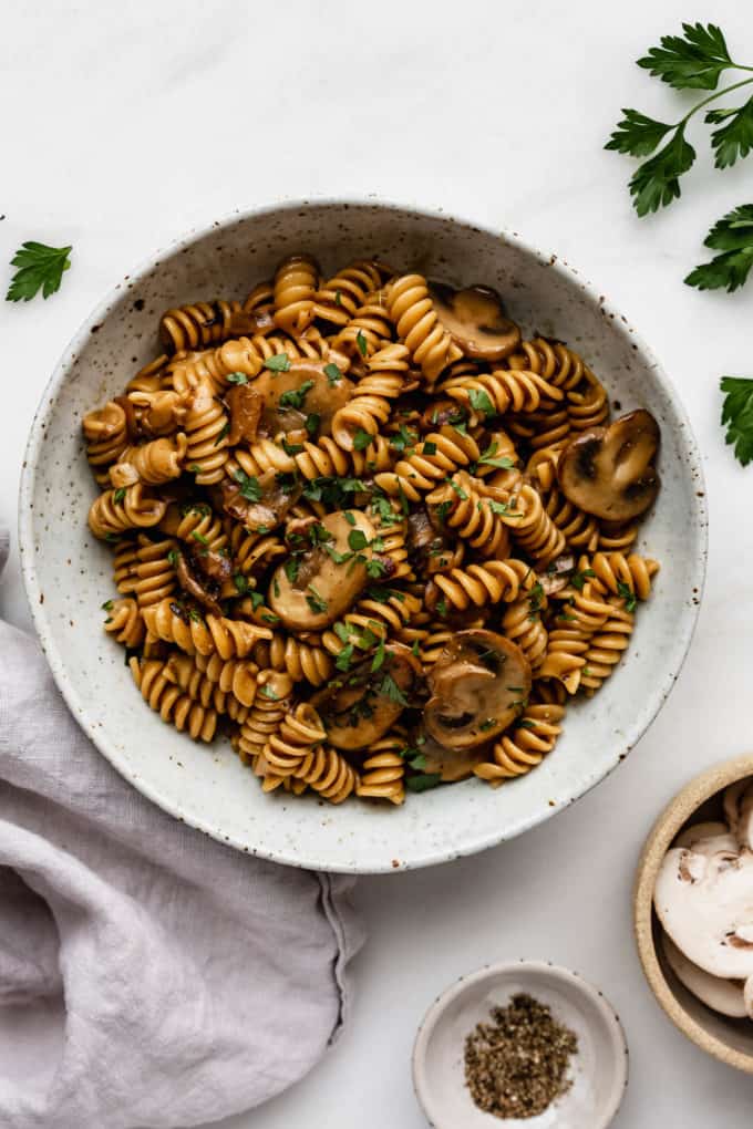 A bowl of mushroom stroganoff with a grey napkin and parsley on the side