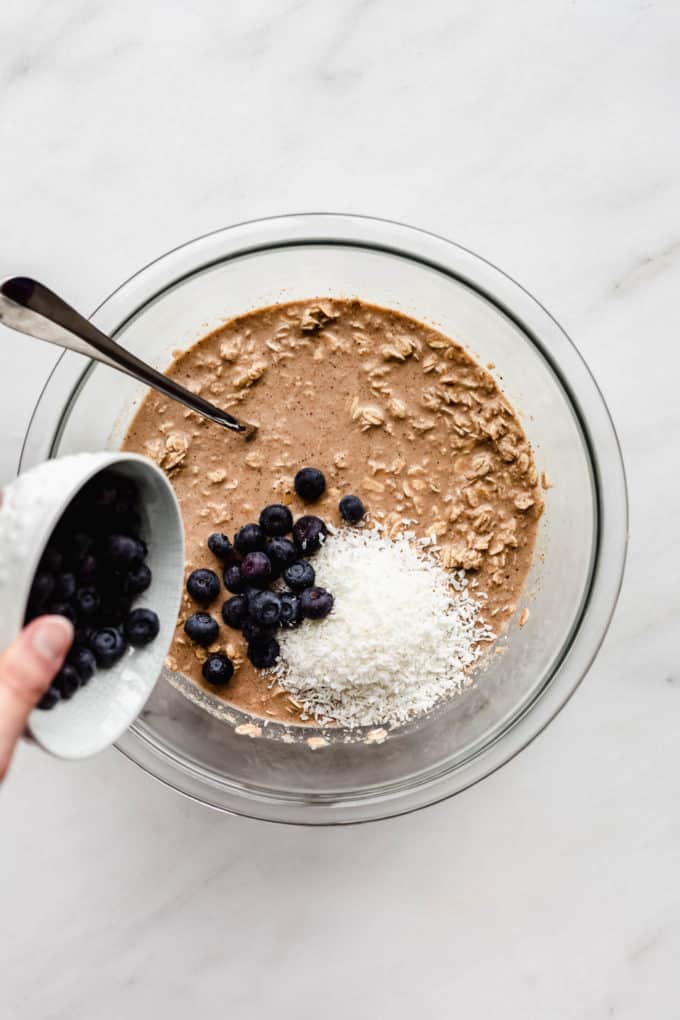 A cup of blueberries being poured into baked oatmeal batter