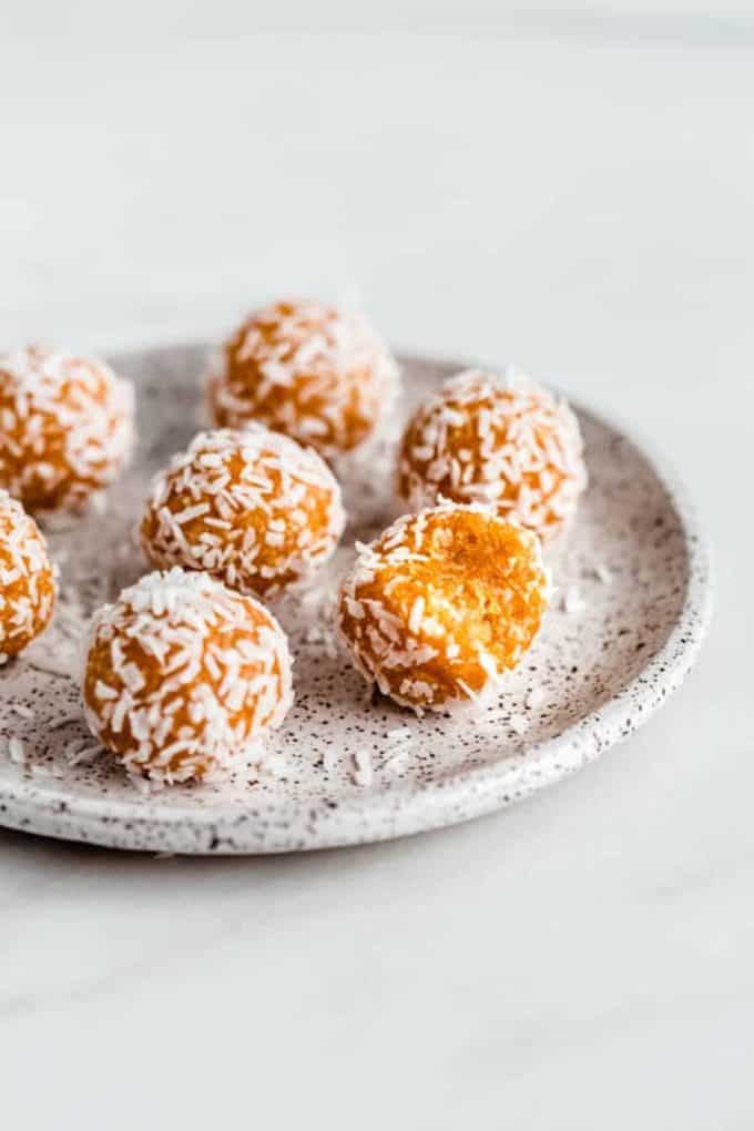 Apricot energy balls topped with coconut on a white speckled plate