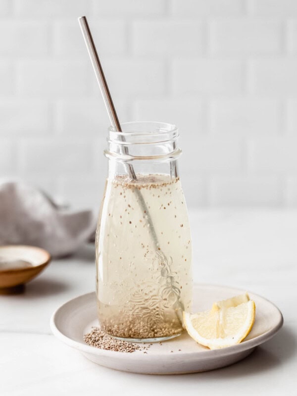 A chia fresca in a glass jar on a white plate with lemons on the side