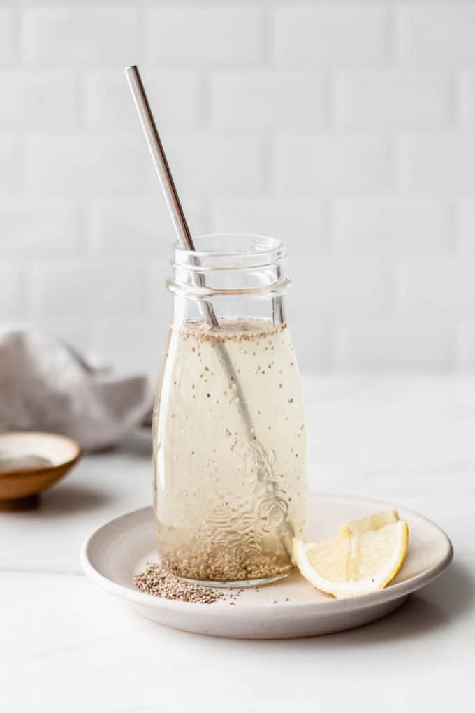 A chia fresca in a glass jar on a white plate with lemons on the side