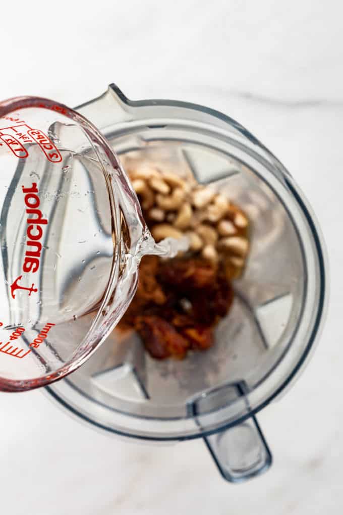 A measuring cup of water being poured into a blender