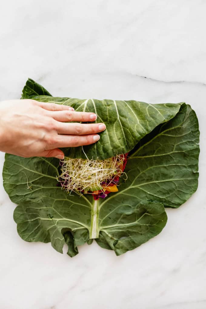 A hand folding a collard green with vegetables inside