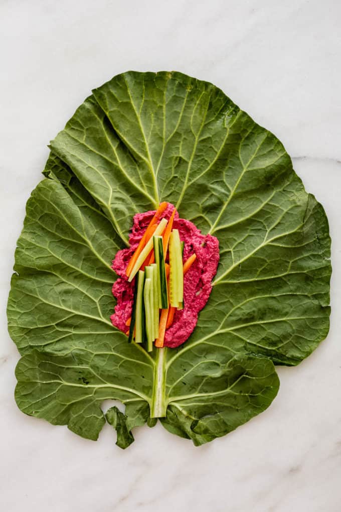 A collard green leaf with beet hummus and cucumber on it