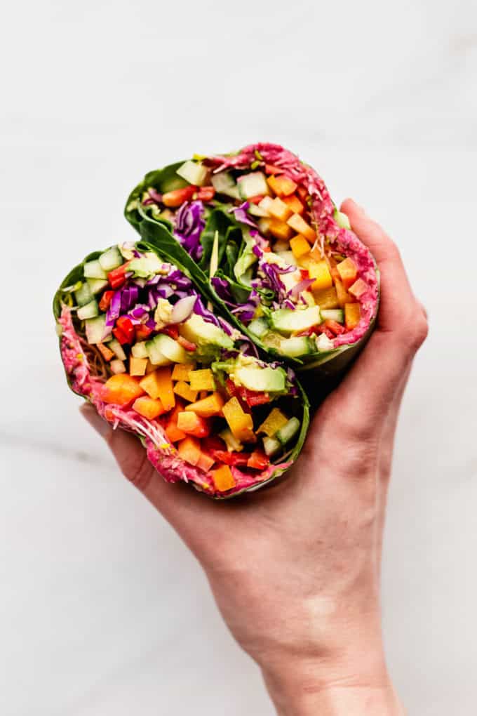 a hand holding a collard green rainbow sandwich wrap