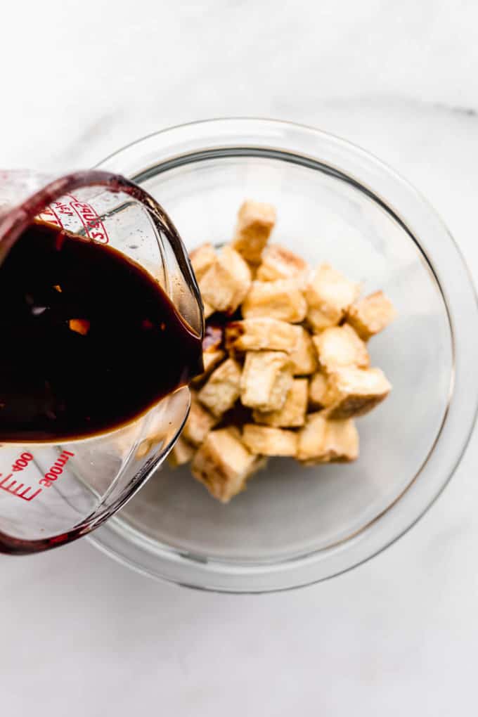 Teriyaki sauce being poured into a bowl of tofu