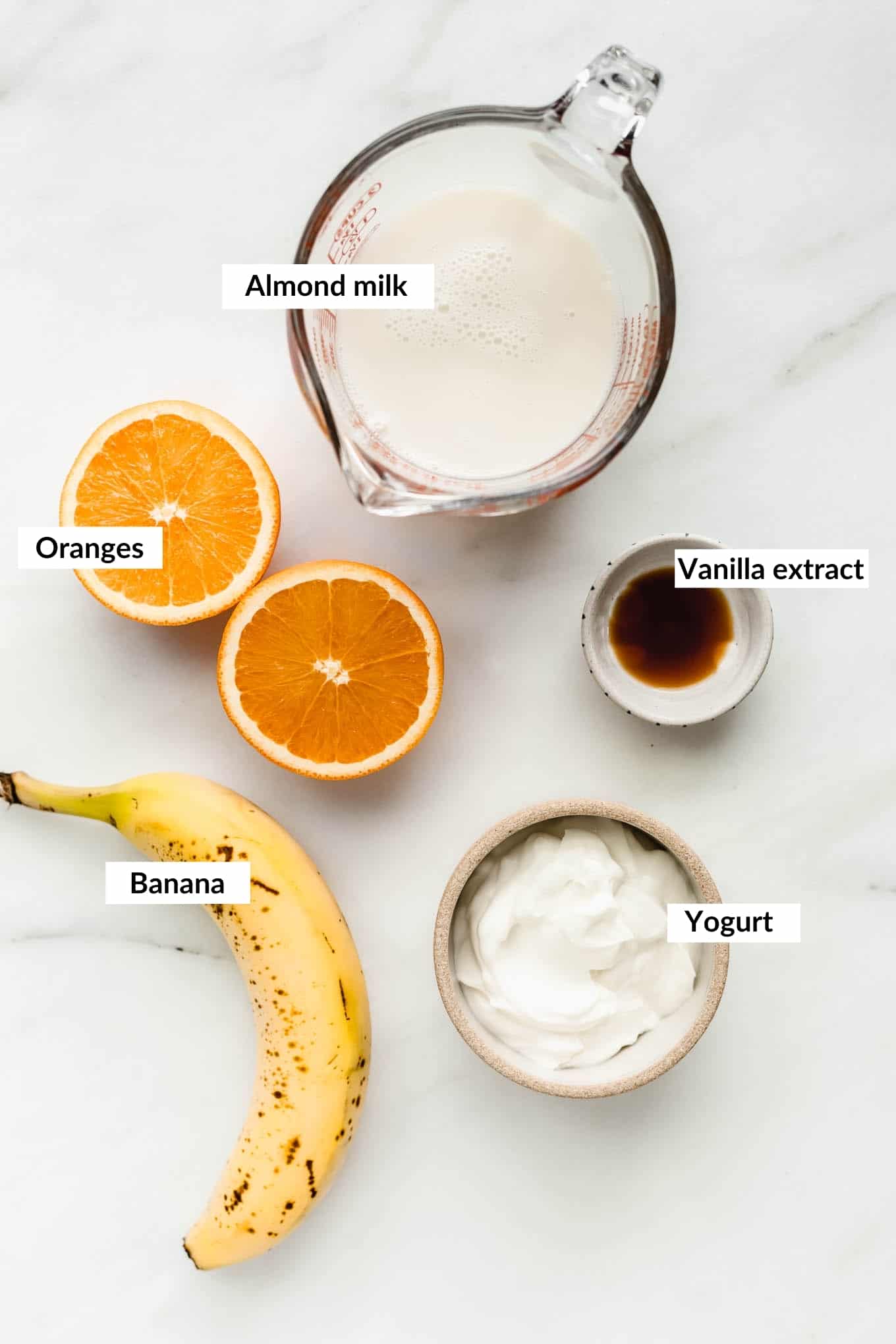 Almond milk, Orange, banana, yogurt and vanilla laid out on a white board