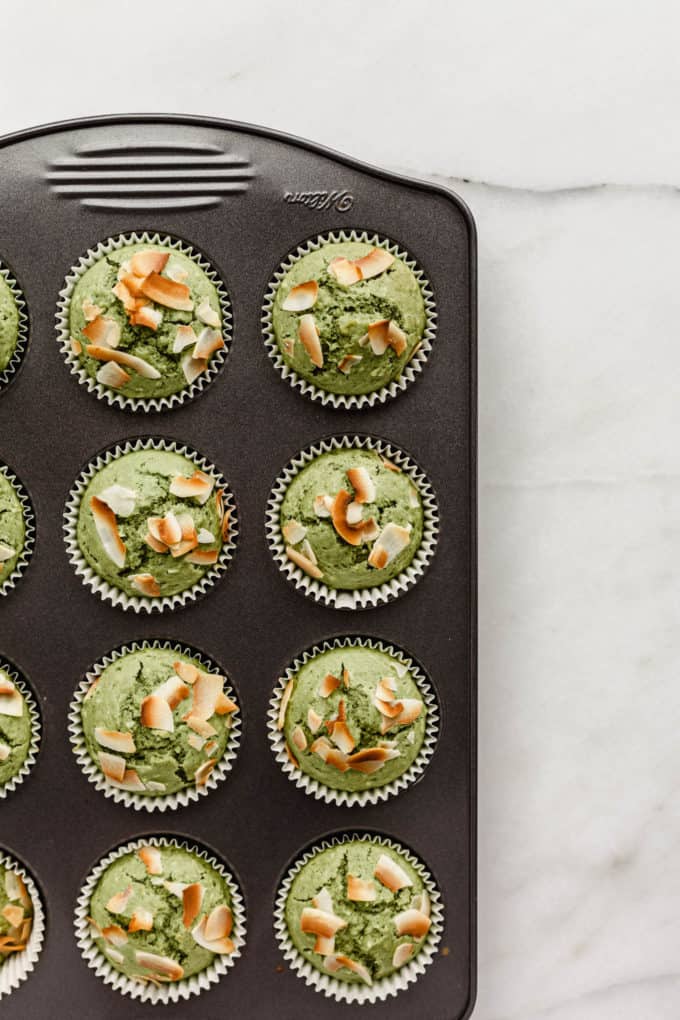 baked matcha muffins topped with coconut in a muffin pan
