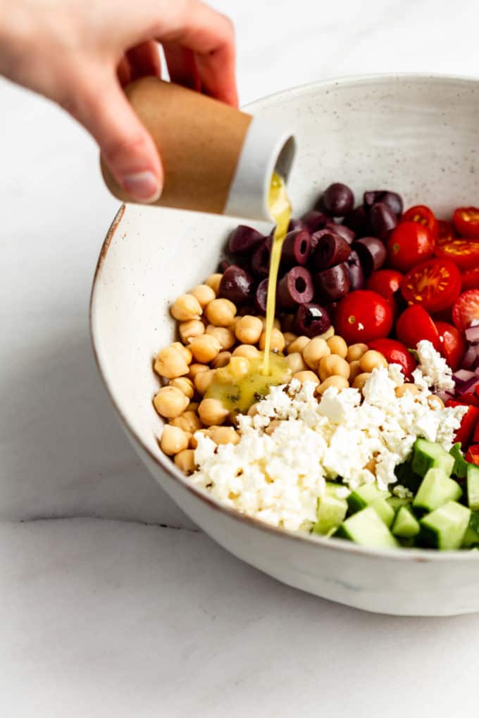 a hand pouring dressing into a bowl of salad