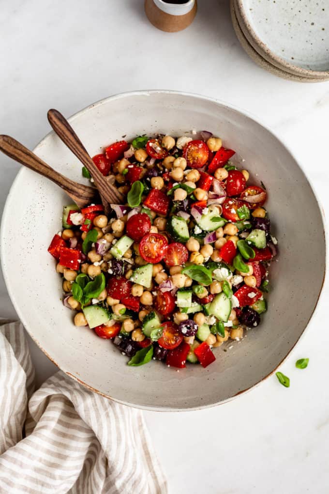 A salad bowl of chickpea salad with a striped beige napkin on the side