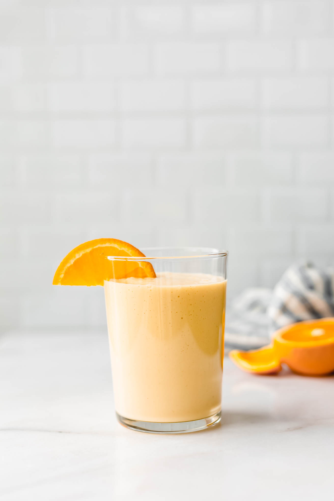 an orange smoothie on a white marble counter with a blue striped napkin