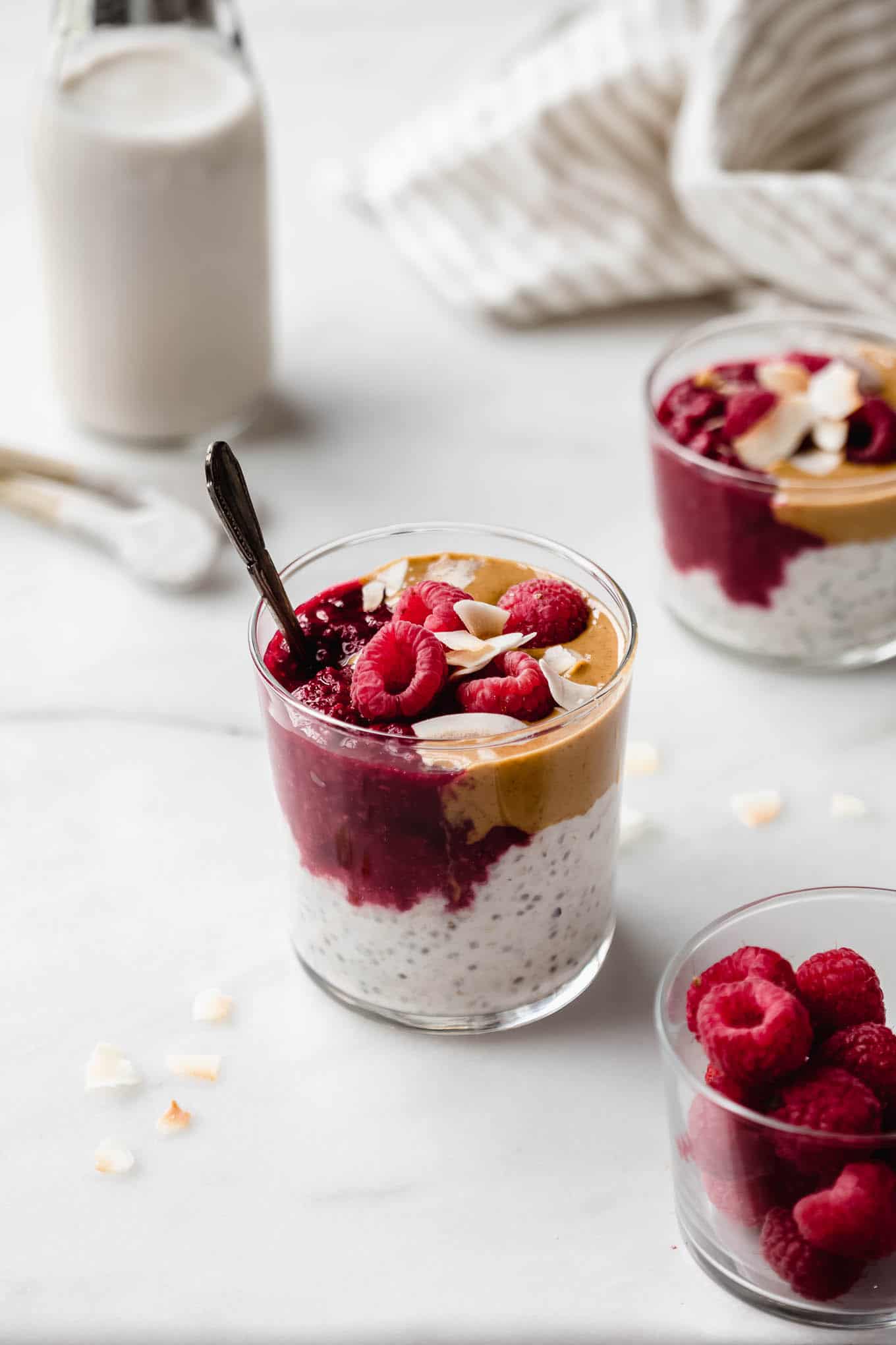 A cup of peanut butter overnight oats with jam and raspberries