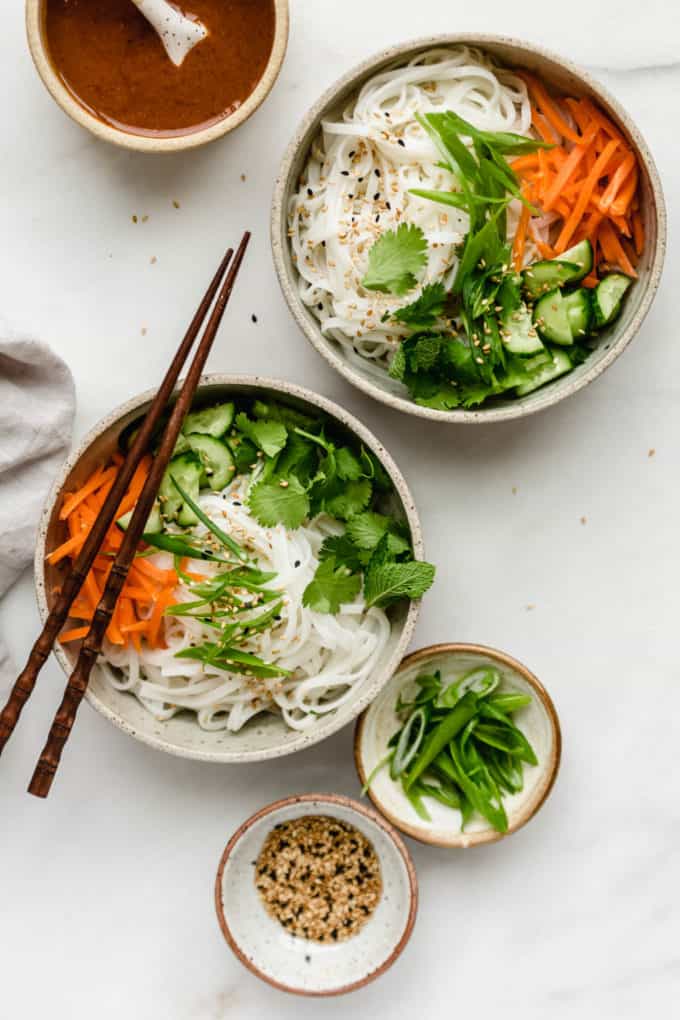 two bowls of rice noodles and vegetables with chopsticks