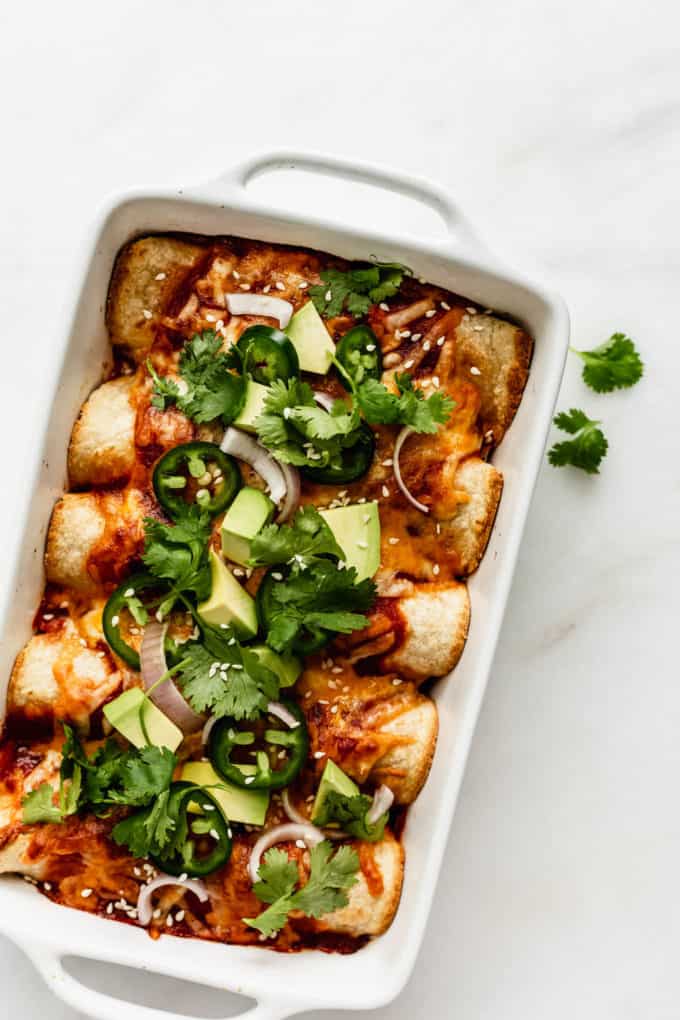 a baking dish of vegetarian enchiladas topped with avocado and cilantro