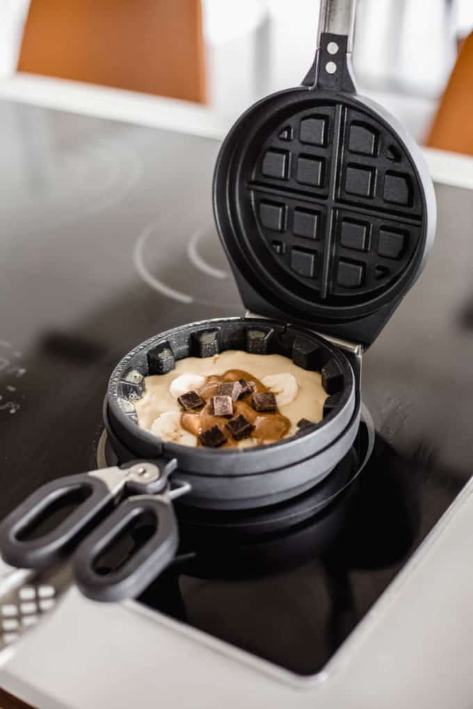 a waffle iron with batter, bananas, chocolate and peanut butter in it