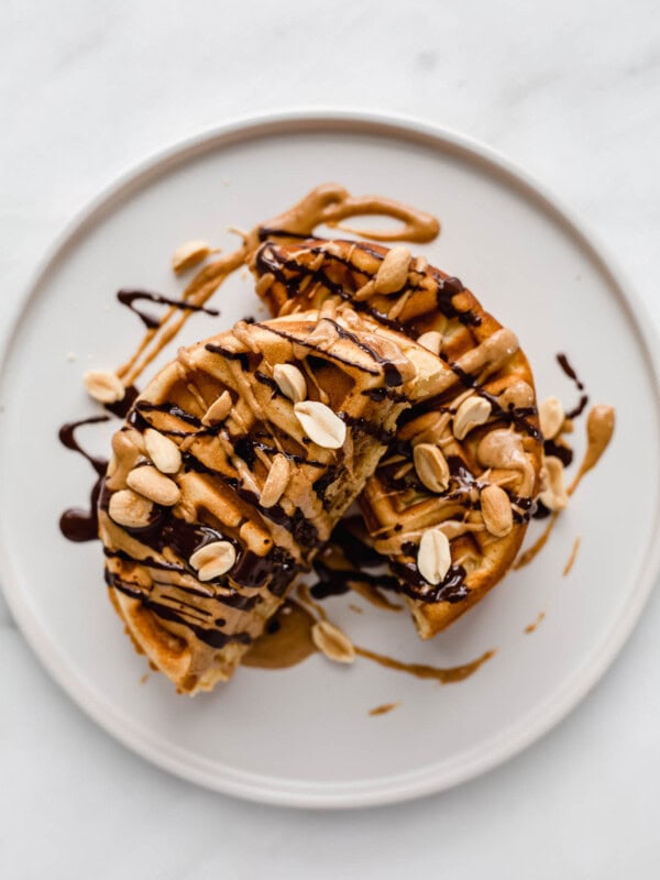 a waffle cut in half on a plate with peanuts and drizzled chocolate on it