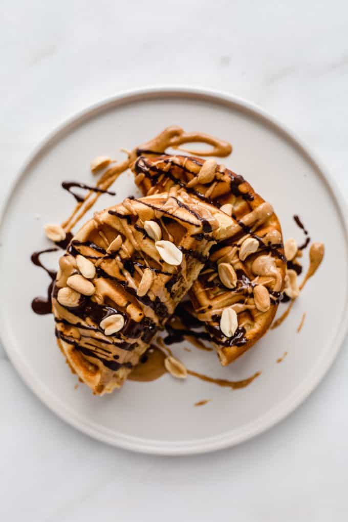 a waffle cut in half on a plate with peanuts and drizzled chocolate on it