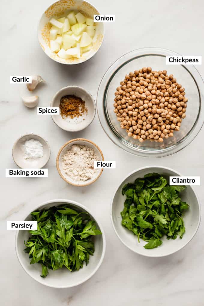 herbs, chickpeas, spices, onions, flour, baking soda and garlic laid out on a marble board