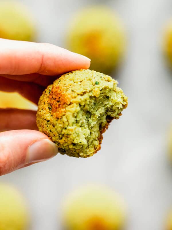 a hand holding a baked falafel ball with a bite taken out of it