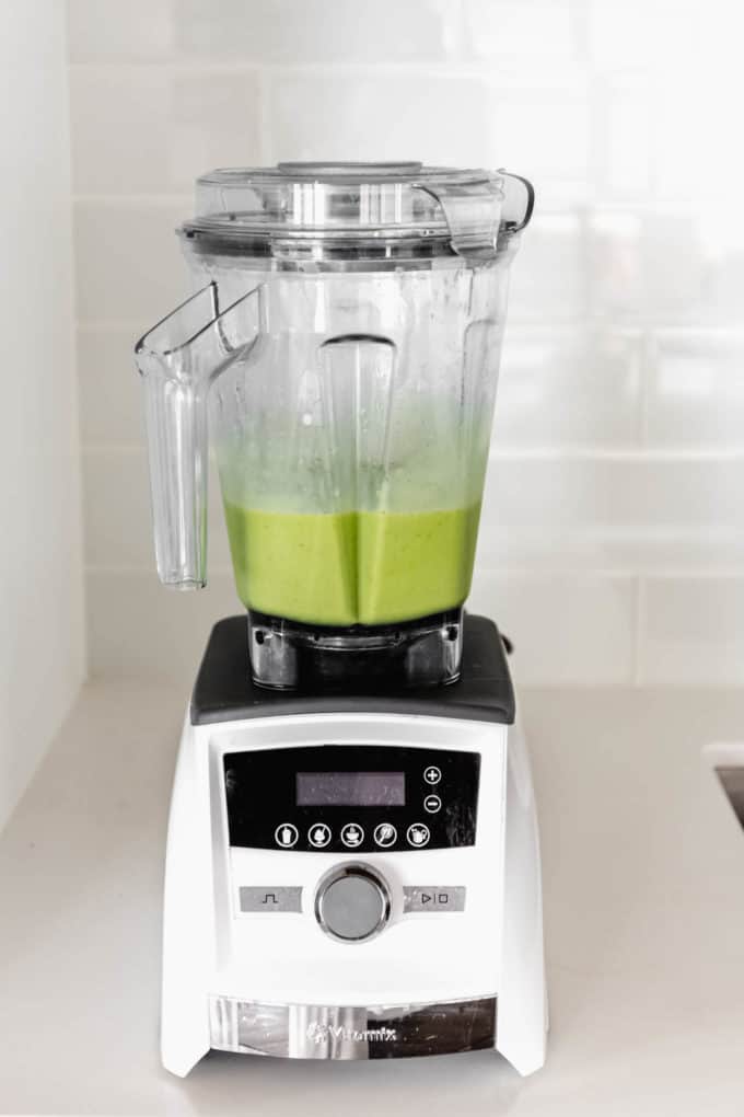 A white blender with a green smoothie in it