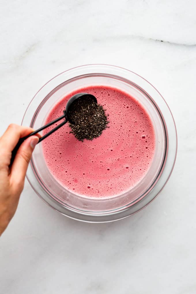 a hand pouring chia seeds into a bowl of raspberry almond milk