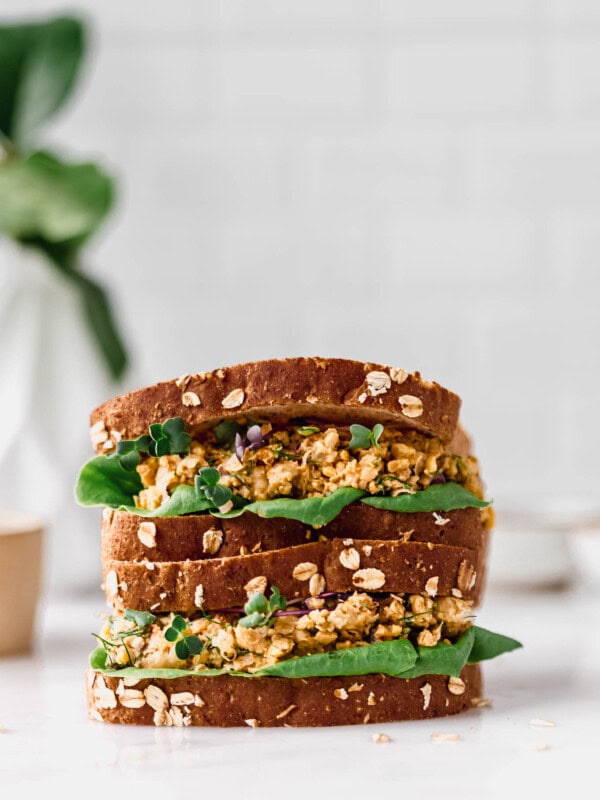 two chickpea salad sandwiches stacked on a marble counter