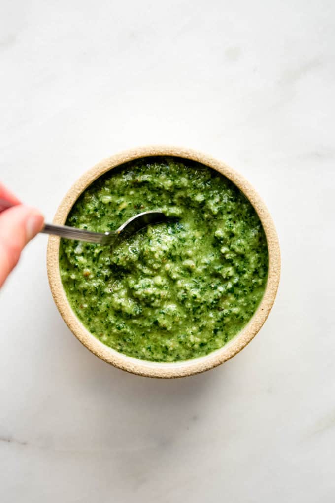 A had holding a spoon in a small bowl of walnut pesto