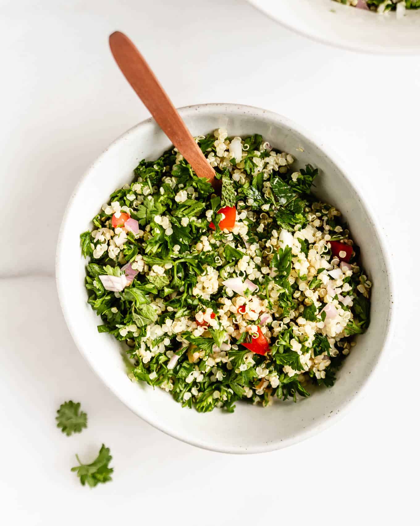 Quinoa tabbouleh salad in a white bowl with a wood spoon