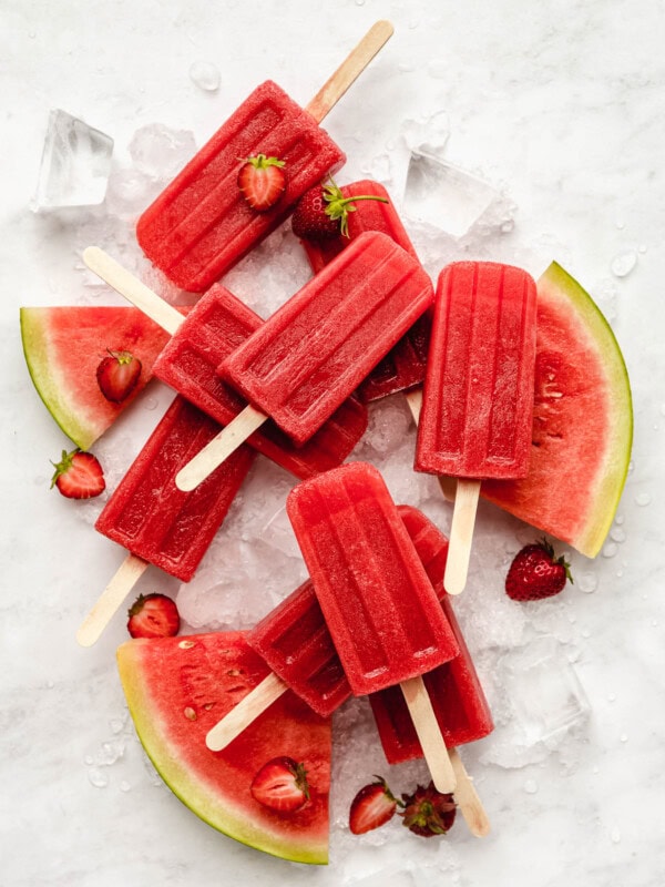 Strawberry watermelon popsicles on a marble board with slices of watermelon