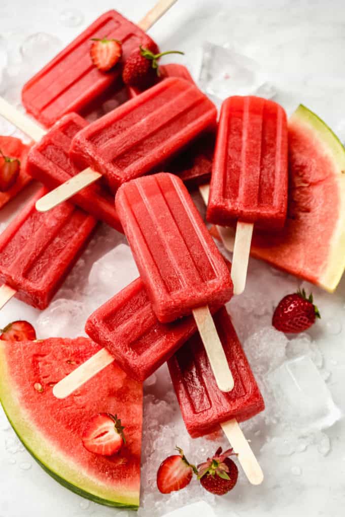 Strawberry watermelon popsicles on ice with strawberries and watermelon around them