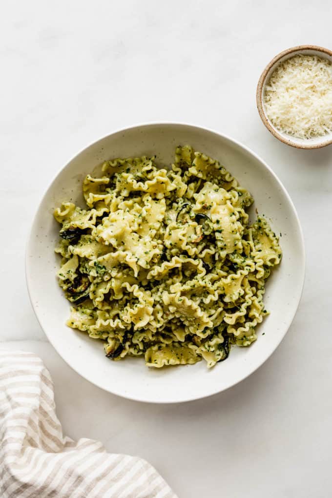 A bowl of veggie pesto pasta with a small bowl of Parmesan cheese on the side