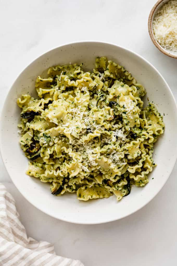 Veggie pesto pasta in a white bowl topped with parmesan cheese