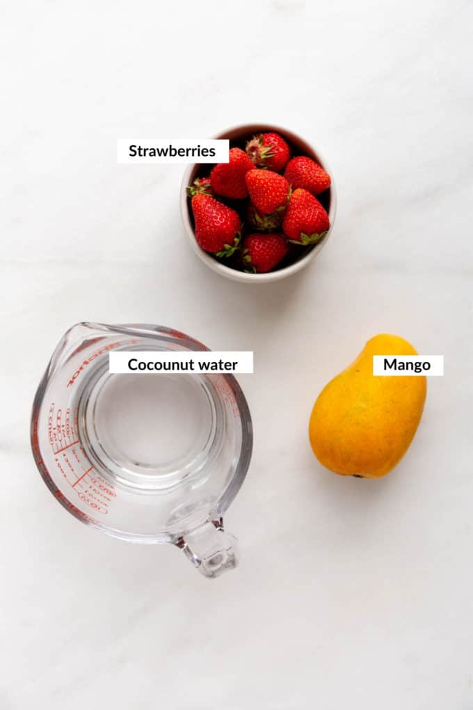 a mango, bowl of strawberries and measuring cup on a marble table