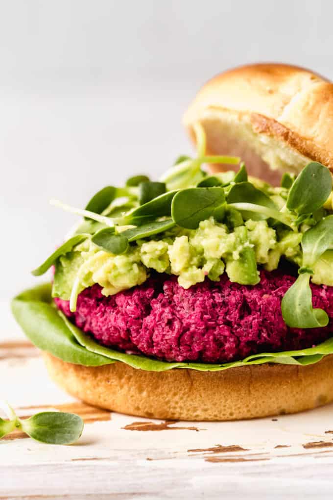A close up of a vegan beet burger topped with mashed avocado and sprouts