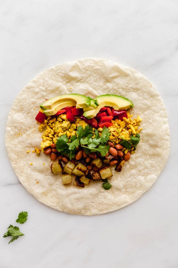 A tortilla with avocado, scrambled tofu and veggies on it