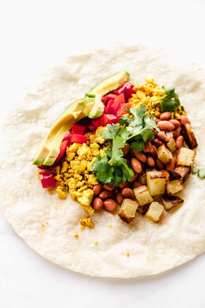 A tortilla with potatoes, beans, tofu, peppers and avocado on it