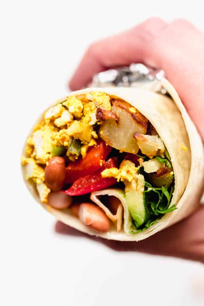 A hand holding a half of a vegan breakfast burrito