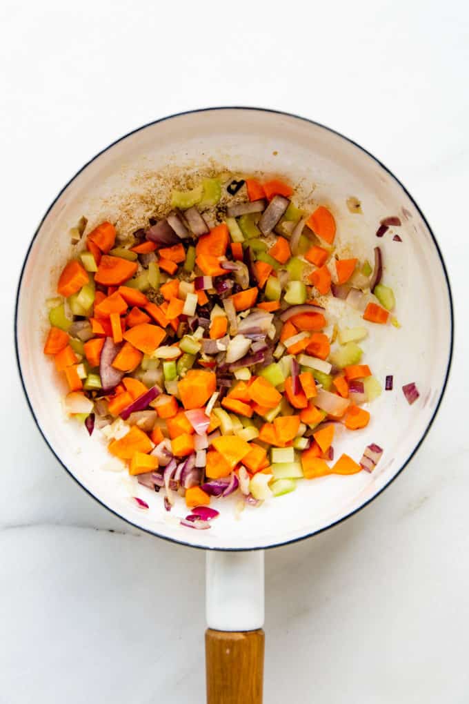 A white pot with carrots, celery and onions in it