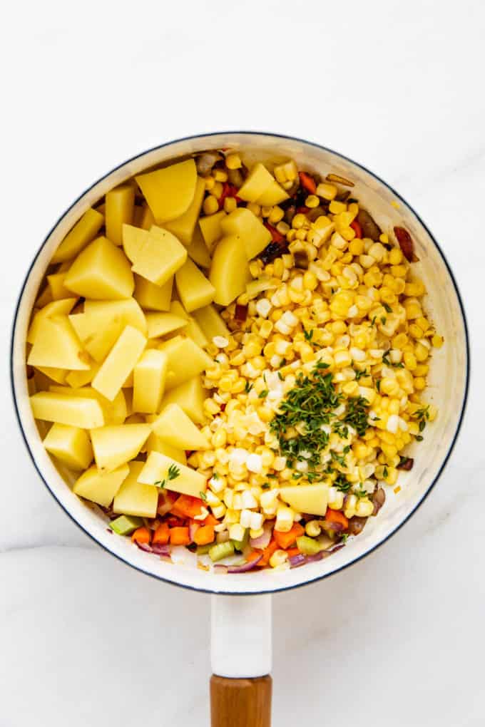 a white pot with potatoes, corn and thyme in it