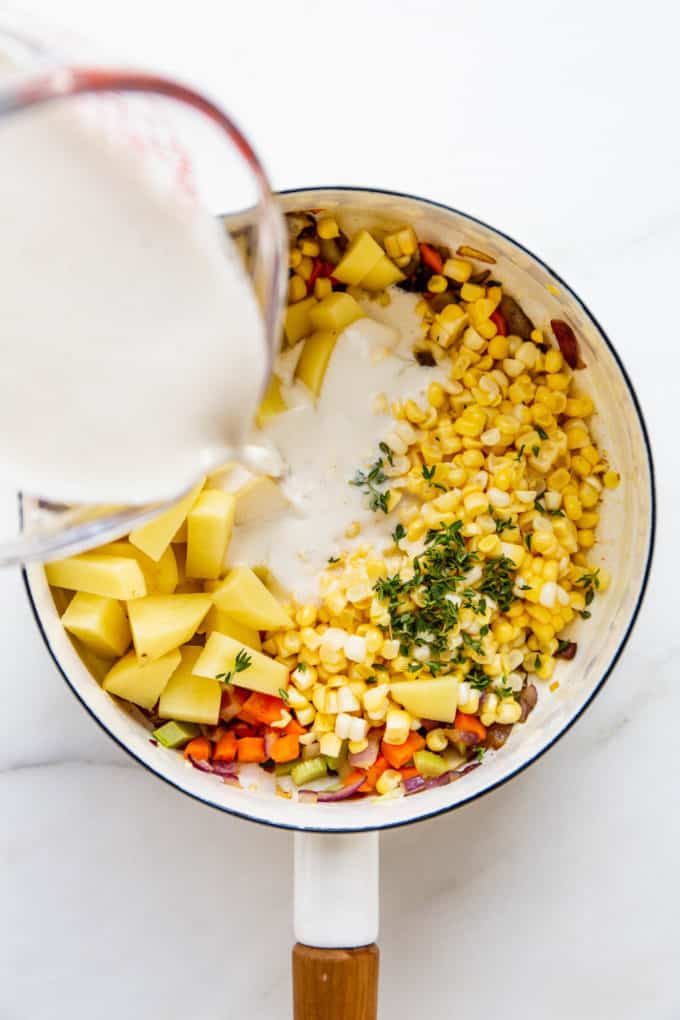 a measuring cup pouring cashew cream into a pot of vegetables
