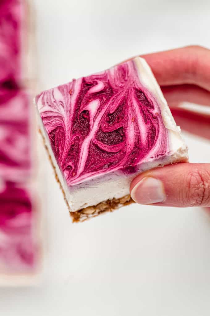 A hand holding a vegan raspberry cheesecake bar