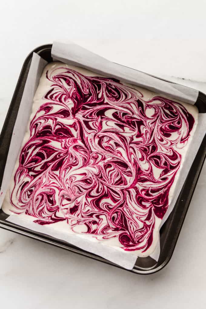 A baking pan with swirled vegan raspberry cheesecake in it